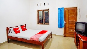 A bedroom with a wooden bed, a television on a wooden stand, a window with metal bars, and a wooden door.