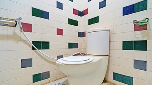 A bathroom with a toilet, tiled walls, and a floor with a pattern of squares. - Flagship 90723 Berlima Guest House Syariah (Malang)