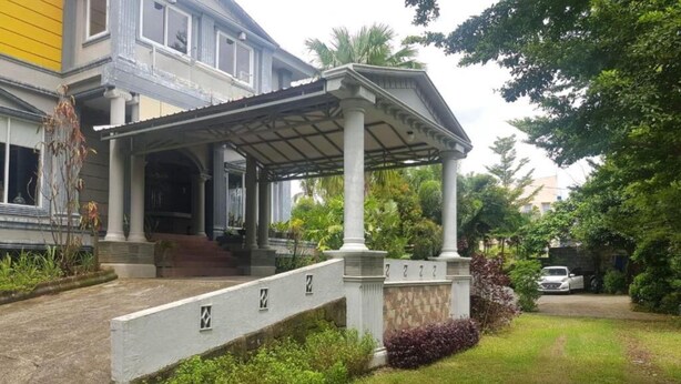 A two-story building with a covered entrance and a stone wall with numbers. - Hotel O Subur (Makassar)