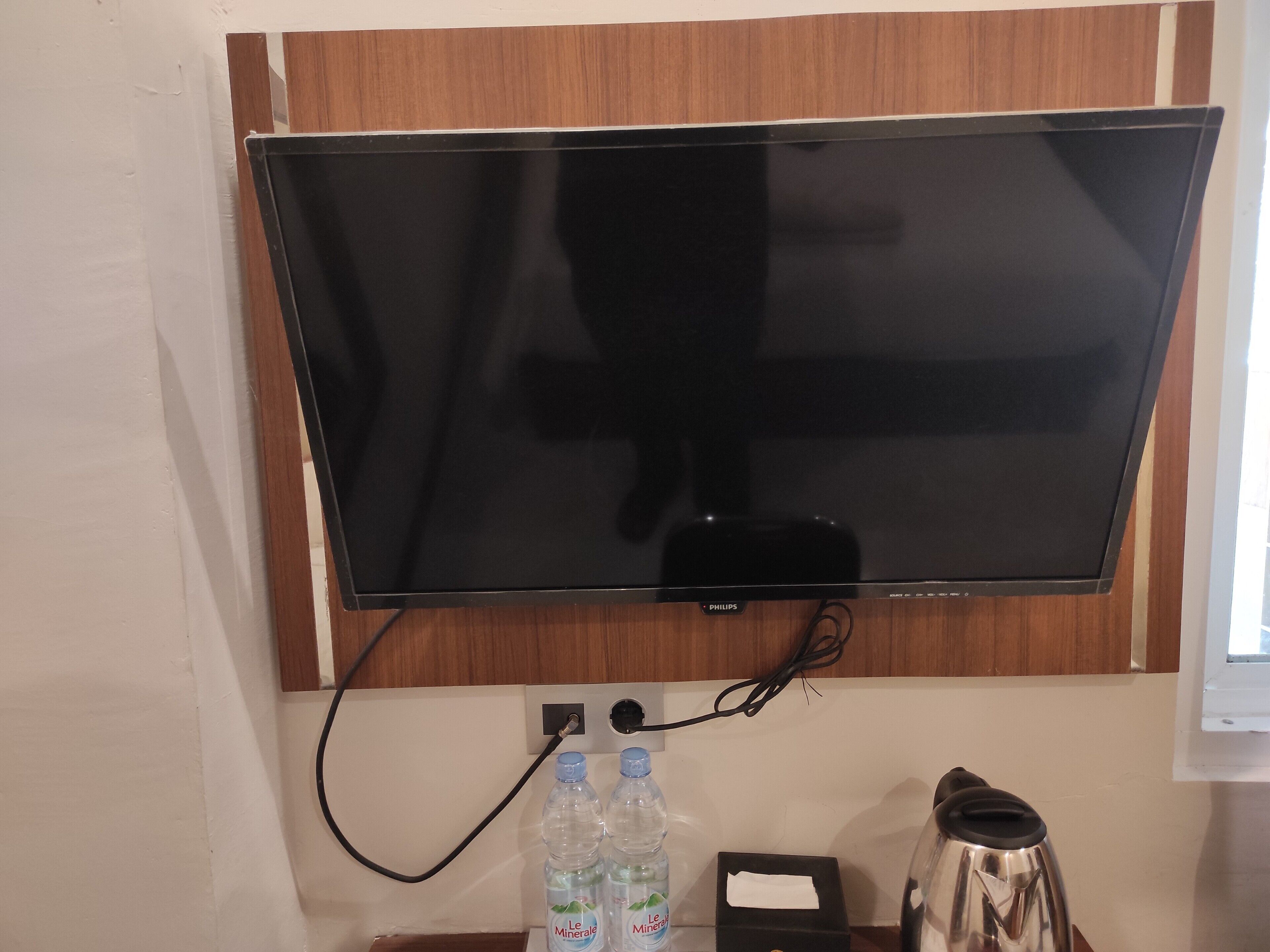 Ein Flachbildfernseher an einer Holzwand befestigt, mit einem Stromkabel und zwei Wasserflaschen mit dem Aufdruck 'Le Minéral' darunter.