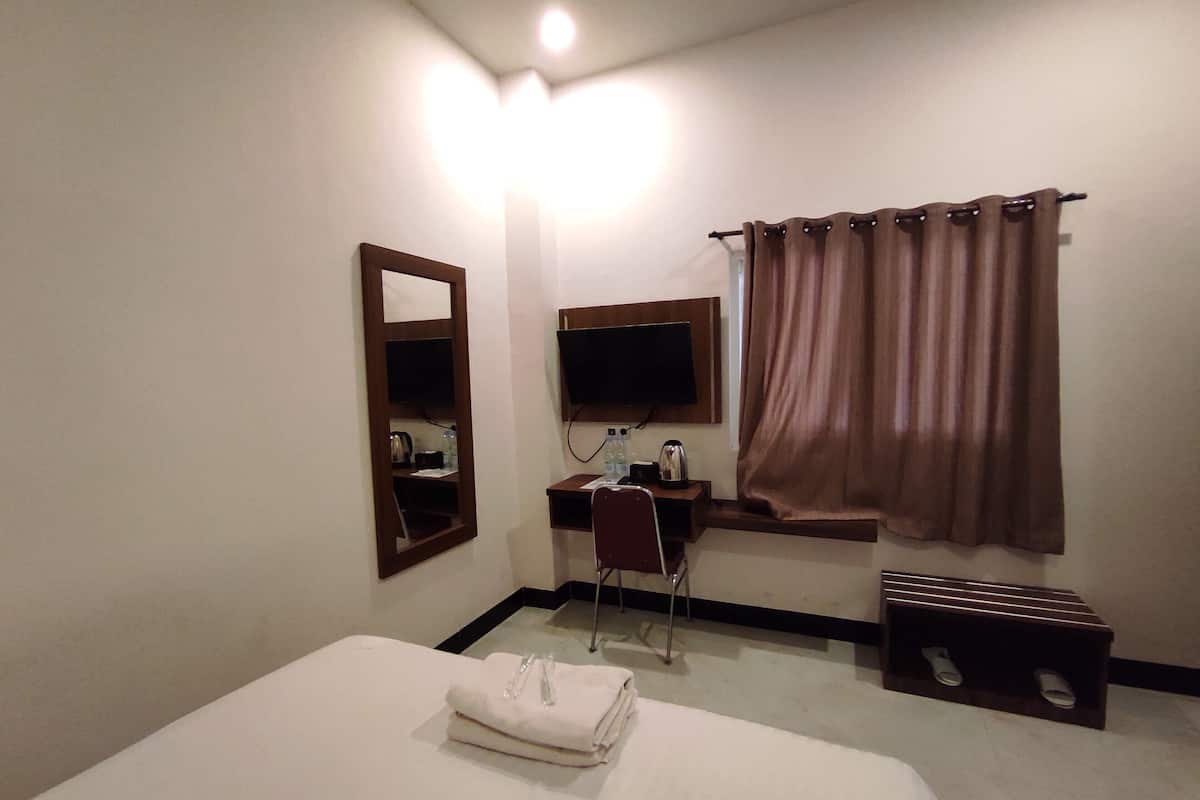 A hotel room with a bed, a desk with a chair, a television, a mirror, and a window with curtains.