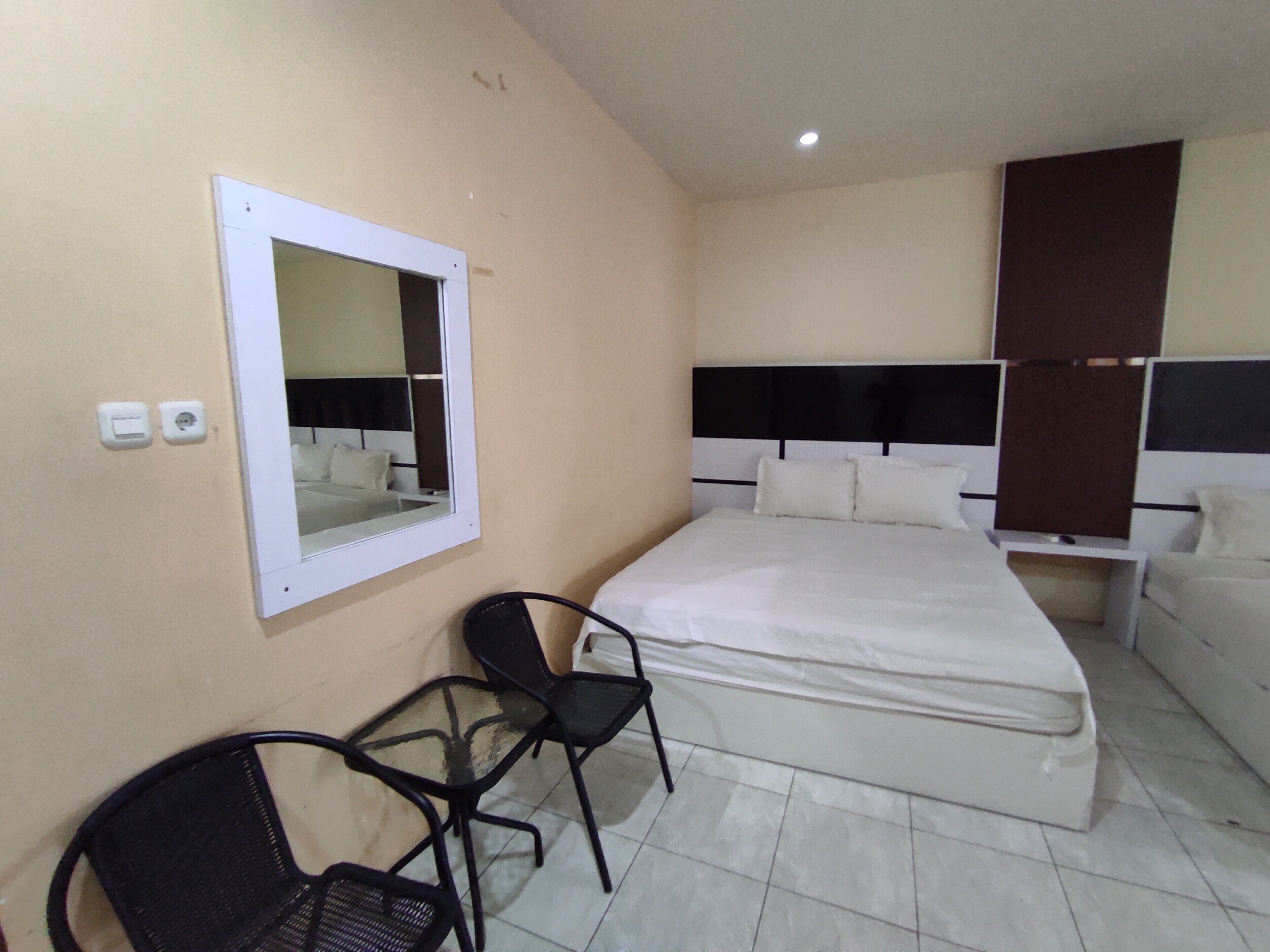 Una camera d'albergo con un letto, una sedia, un comodino, uno specchio e una lampada a parete.
