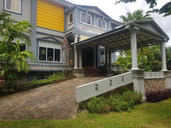A two-story building with a covered entrance and a small garden area. - Hotel O Subur (Makassar)