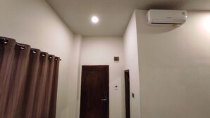 A hallway with a wooden door, a white wall, and an air conditioning unit mounted on the wall. - Hotel O Subur (Makassar)