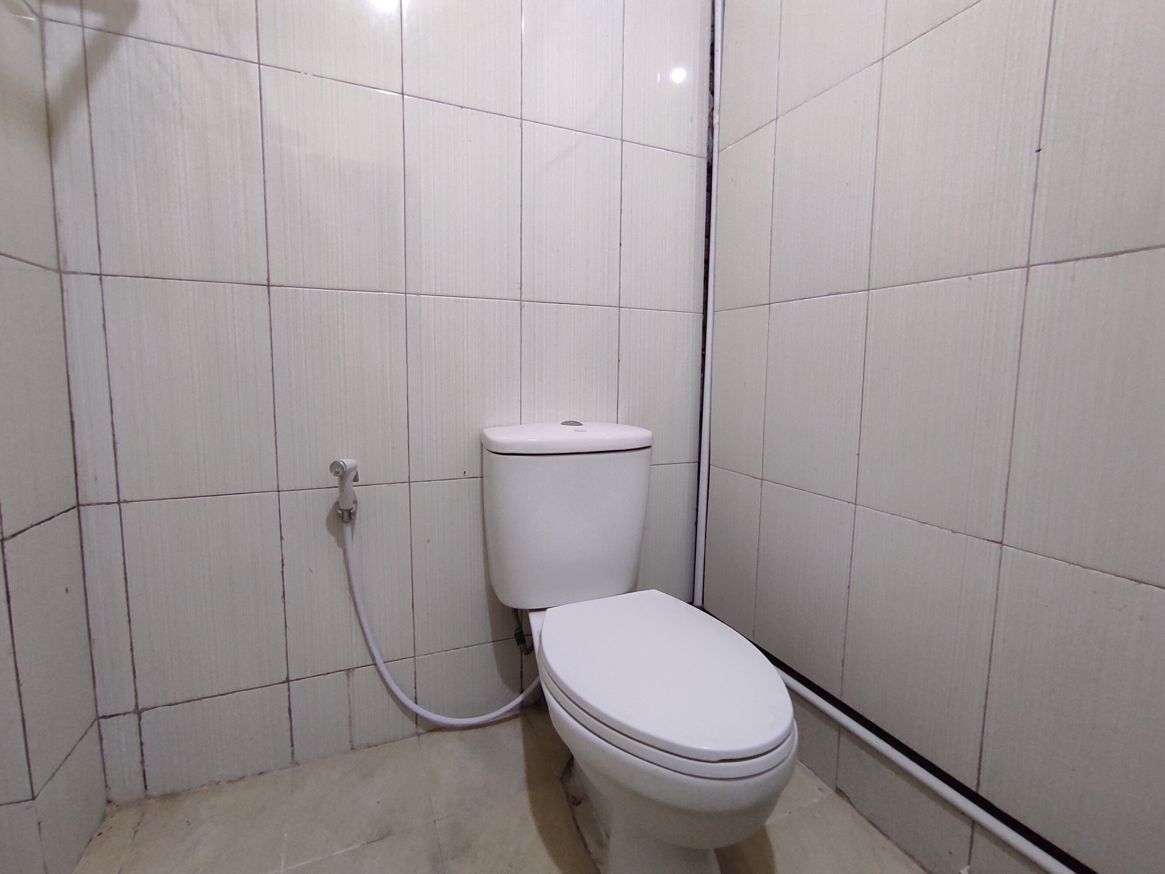 Un baño pequeño con azulejos blancos, que incluye un inodoro y una tubería visible.