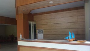A reception desk with a wooden finish, a calendar, and a small decorative sailboat model. - Hotel O Subur (Makassar)