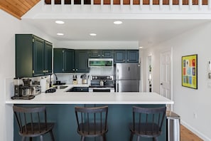 A modern kitchen with dark green cabinets, stainless steel appliances, and a white island with bar stools.