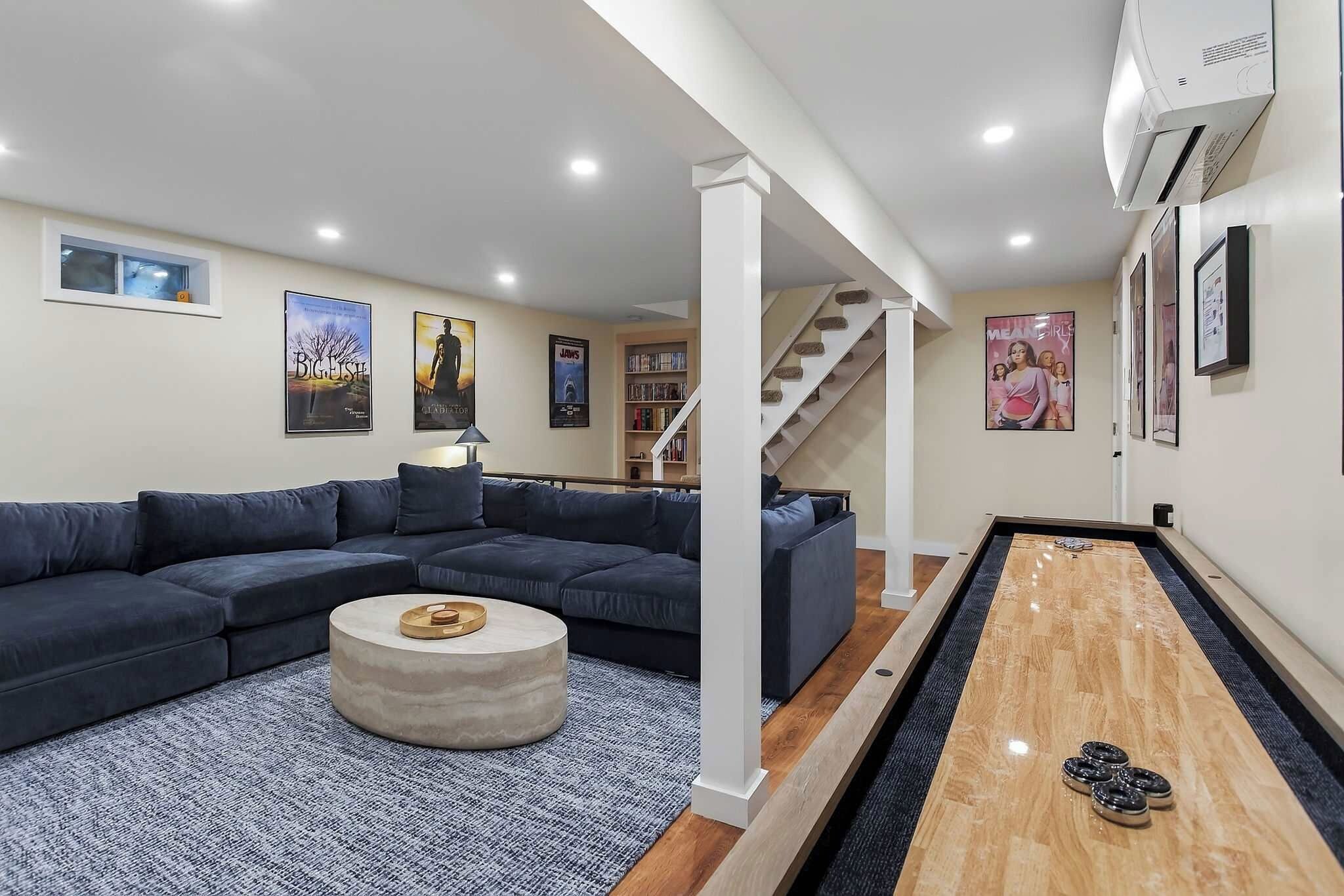 Una sala de estar moderna con un sofá modular, una mesa de centro, una mesa de billar y una escalera que lleva a otro nivel.