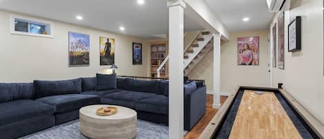 Una sala de estar moderna con un sofá modular, una mesa de centro, una mesa de billar y una escalera que lleva a otro nivel.