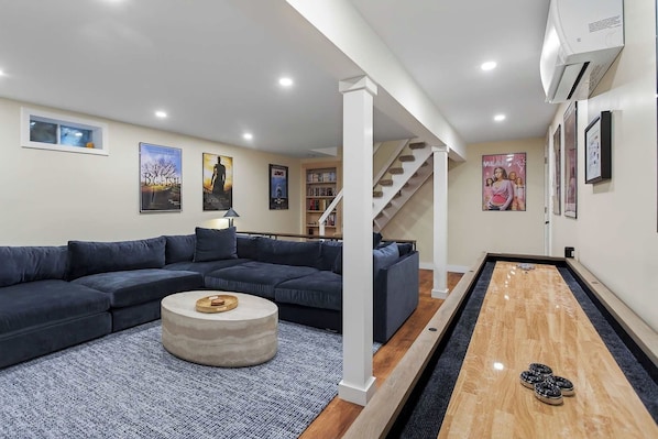 A modern living room with a sectional sofa, a coffee table, a pool table, and a staircase leading to another level.