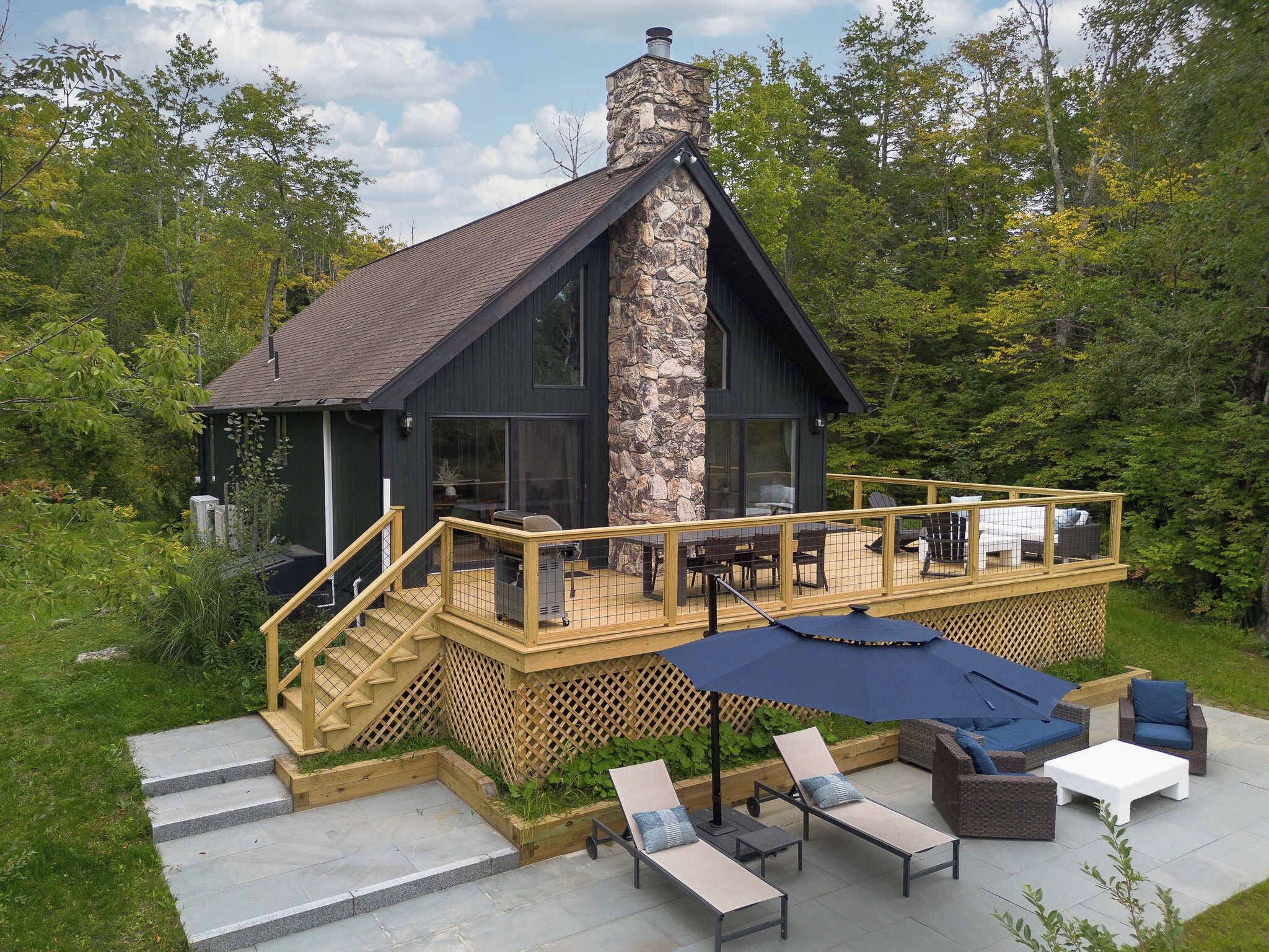Een modern huis met een stenen schoorsteen, een terras met buitenmeubilair en een trap naar de ingang.