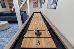 A shuffleboard table with the number 3 visible, a blue couch, and a staircase in the background.
