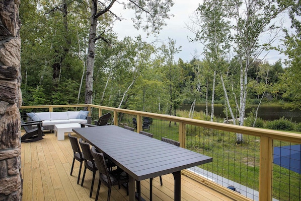 An outdoor deck with a table and chairs, surrounded by a wooden railing and overlooking a lake.