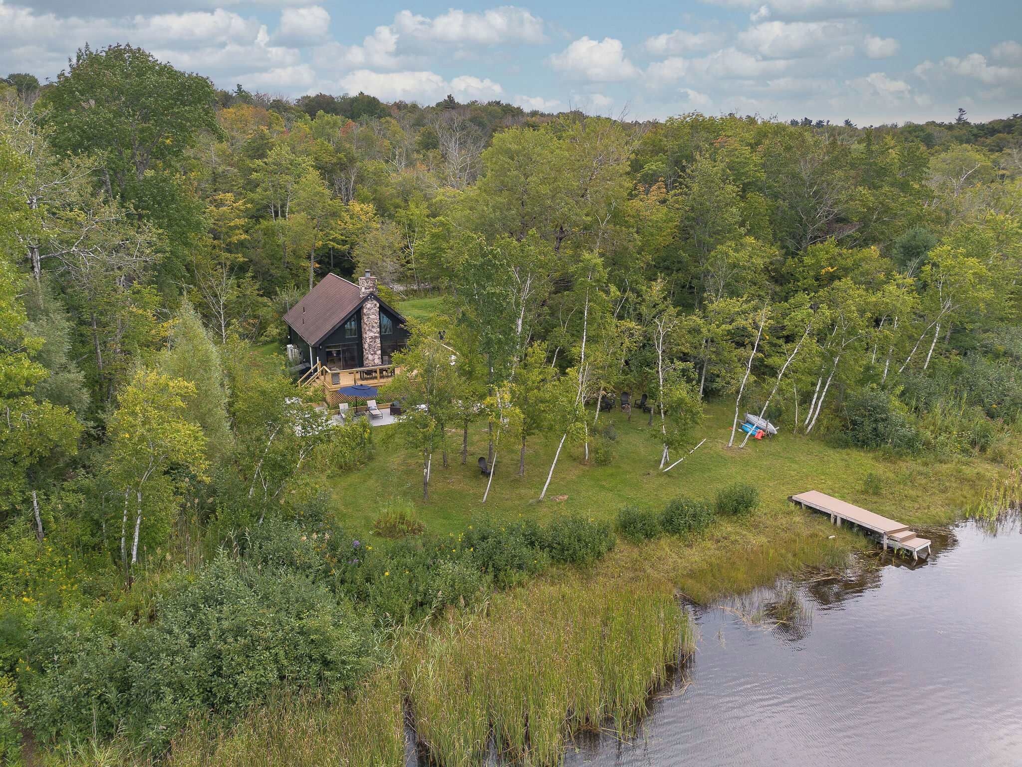 Eine Holzhütte mit einer Terrasse und einem Steg, der in einen See führt, umgeben von dichtem Wald.
