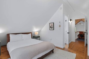Un dormitori amb llit, taula de nit, làmpada i una porta que condueix a una altra habitació.
