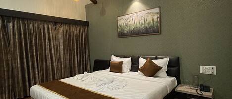 A neatly made bed with a brown headboard, a painting of a forest on the wall, and a nightstand with a phone and a lamp.