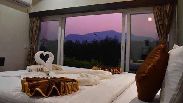 A hotel room with a large bed, a view of mountains at dusk, and a window with curtains.
