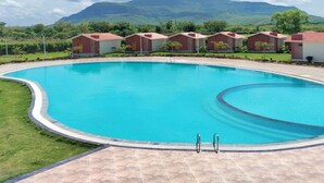 A swimming pool with a curved edge, surrounded by a paved deck. In the background, there are several small buildings with red roofs, likely part of a resort or hotel.
