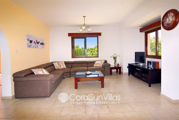 A living room with a sectional sofa, a coffee table, a TV, and a clock on the wall.