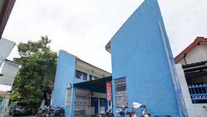 Een blauw gebouw met een hek, geparkeerde motorfietsen en een auto.