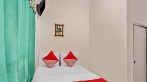 Een slaapkamer met een bed, twee kussens, een rode deken, een aan de muur bevestigde televisie en een klein fotolijstje.