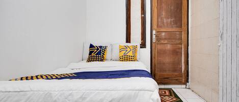 Een slaapkamer met een bed, kussens, een houten deur en een kamerkleed met dessin.