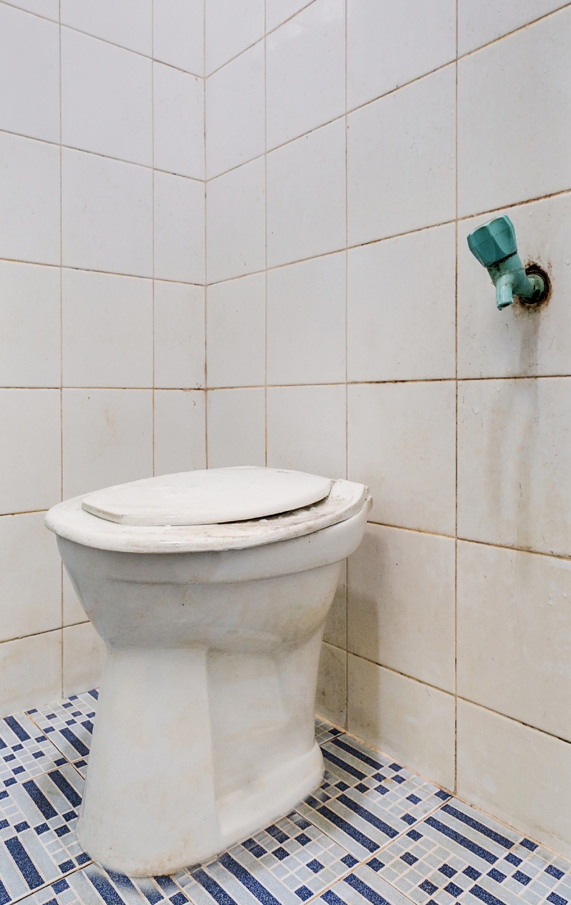 A toilet in a bathroom with white tiles and a blue and white patterned floor.