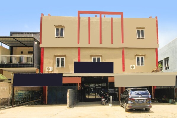 A multi-story building with a flat facade, a covered entrance, and a parked car.
