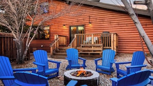 Una cabaña de troncos con un brasero y sillas Adirondack azules dispuestas alrededor.