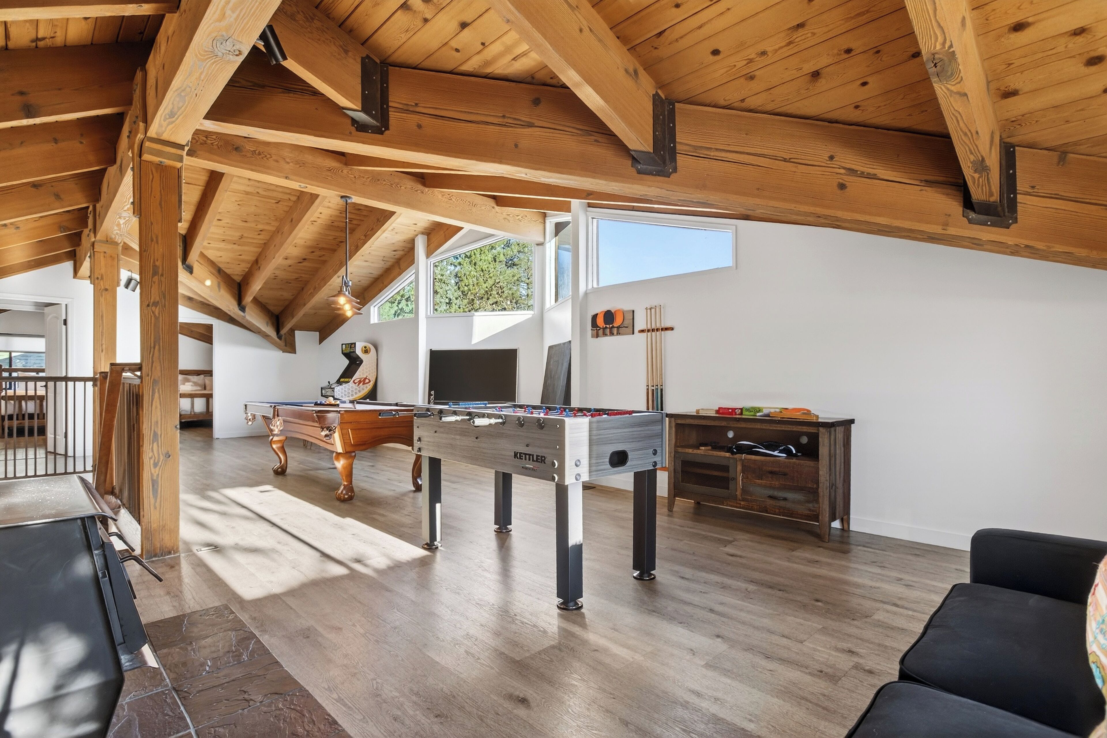 Una habitación amplia con techo de madera, mesa de fútbol de mesa, mesa de billar y un soporte para tacos de billar.