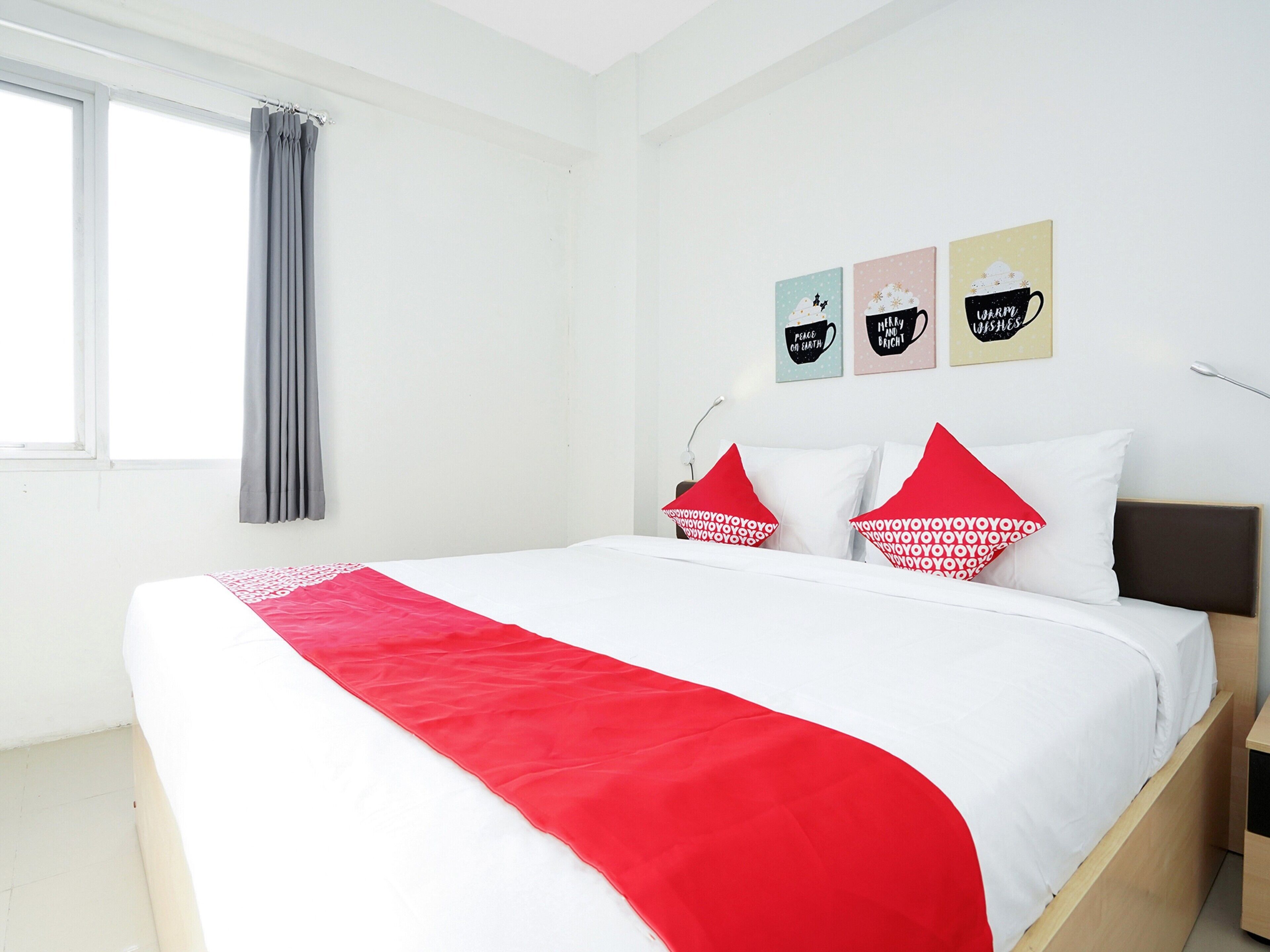 A neatly made bed with a red blanket, white pillows, and a grey curtain.