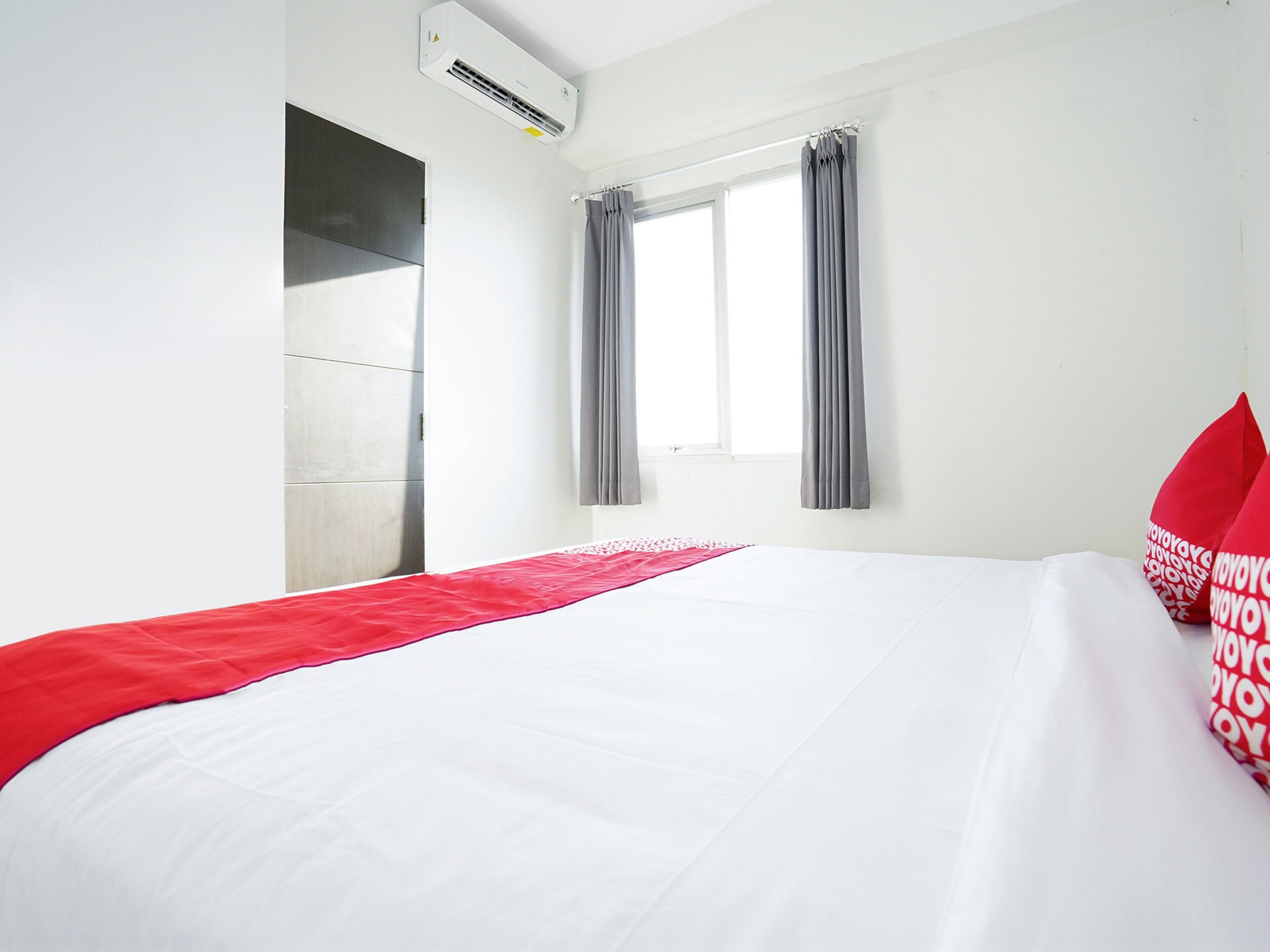 A hotel room with a bed, a window with curtains, an air conditioning unit, and a wall-mounted wardrobe.