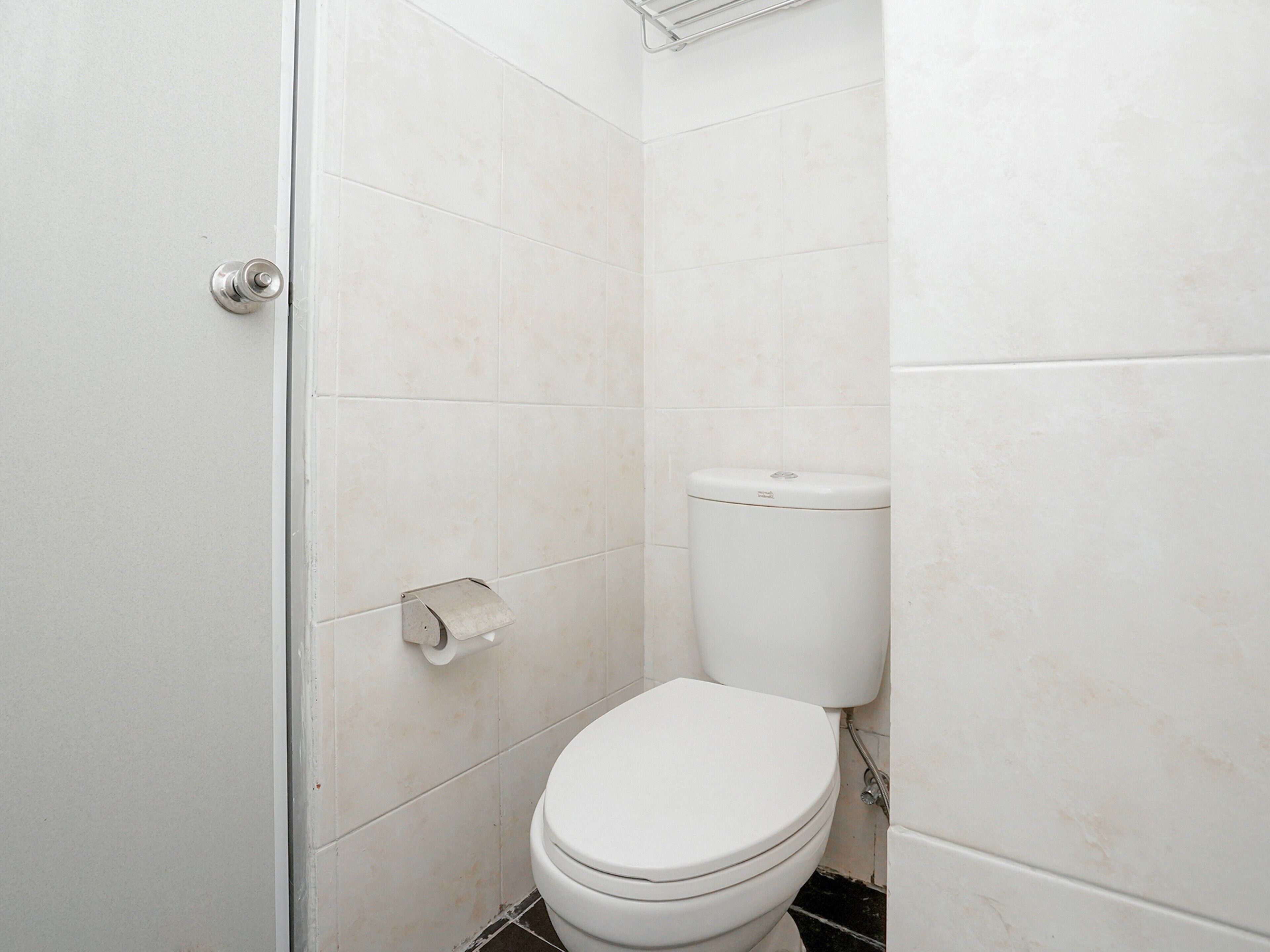 Ein kleines, weißes Badezimmer mit Toilette, Papierhandtuchspender und Duschbereich.