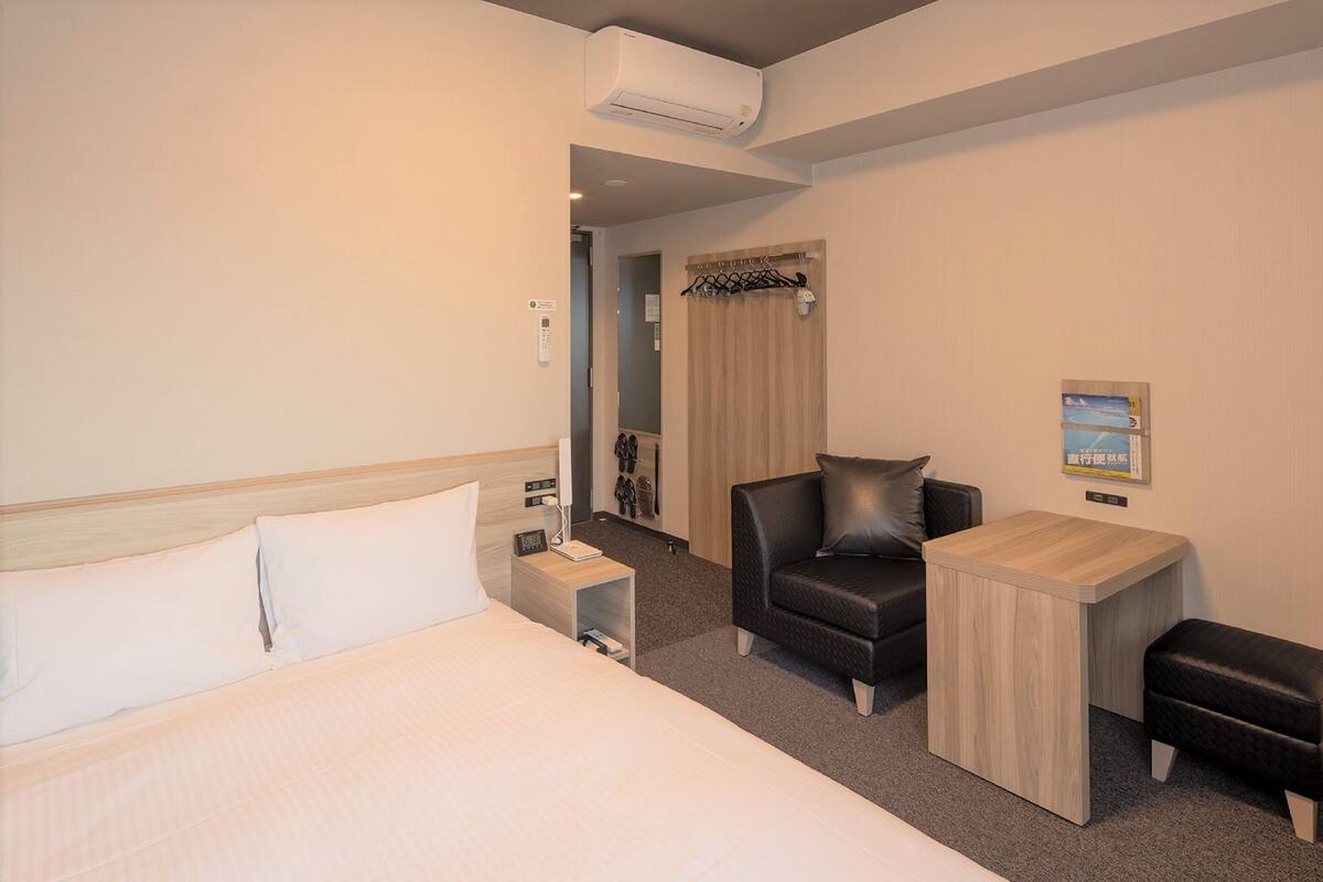 A hotel room with a bed, a chair, a small table, and a coat rack.