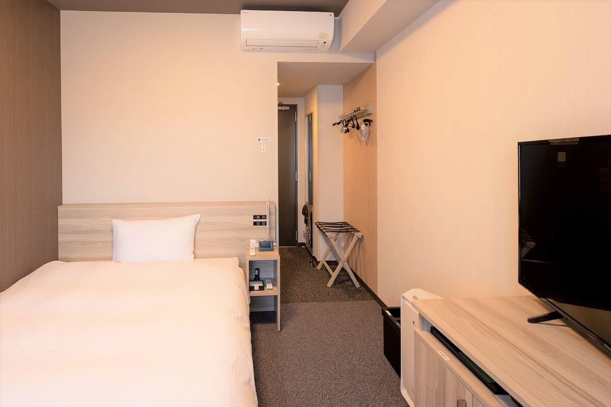A hotel room with a bed, bedside table, TV, and a small seating area with a chair and a table.
