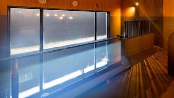 Una piscina interior moderna con pared de vidrio, paneles de madera y un rincón iluminado por el sol.