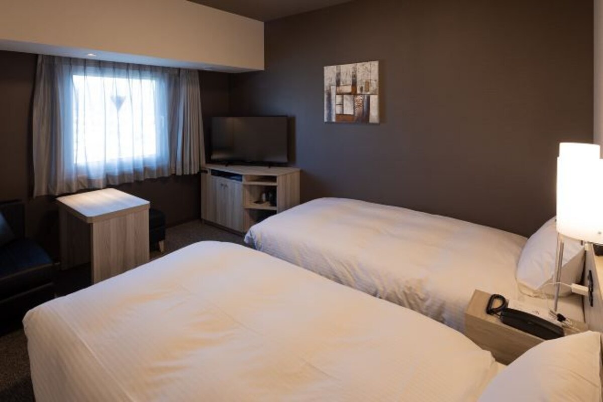 A hotel room with two beds, a desk, a television, and a painting on the wall.