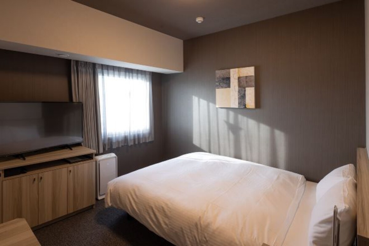 A hotel room with a bed, a TV, a cabinet, and a window with curtains.
