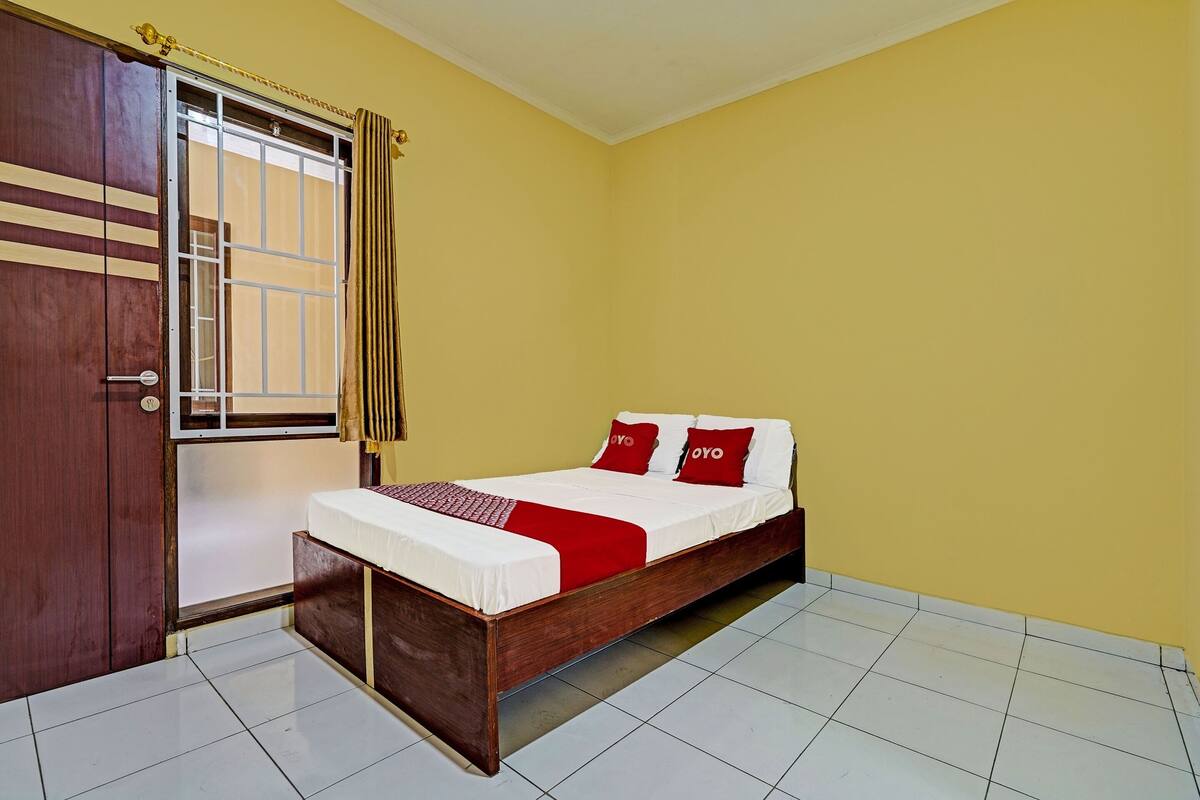 A bedroom with a wooden bed, a red and white bedspread, and a yellow wall.
