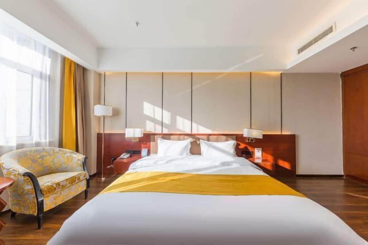A hotel room with a large bed, a nightstand, a lamp, a chair, and a window with curtains.