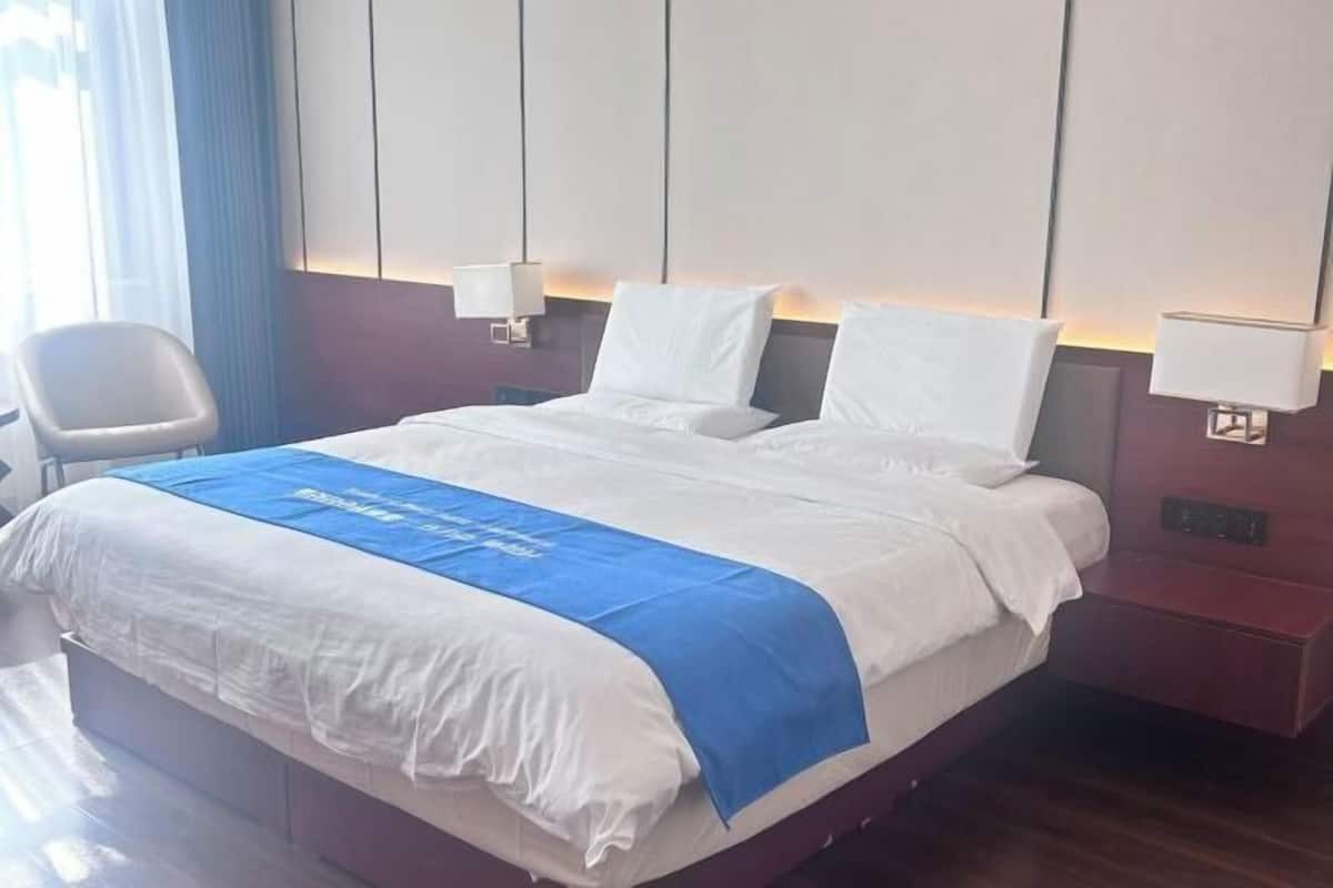 A hotel room with a large bed, two bedside tables, a chair, and a blue bed runner.