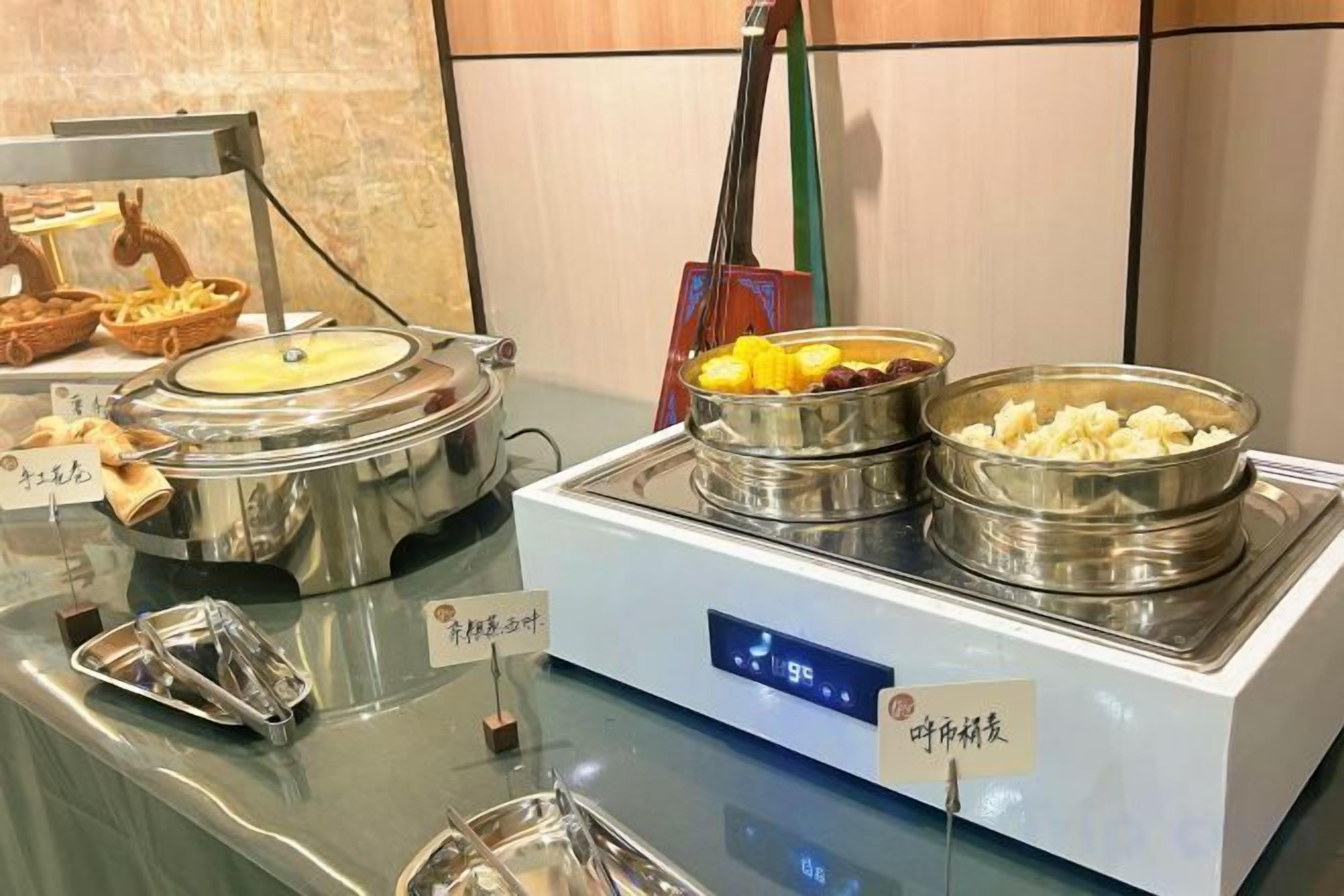Montaje de bufé con diversos alimentos en recipientes metálicos, un reloj digital y un letrero con texto.