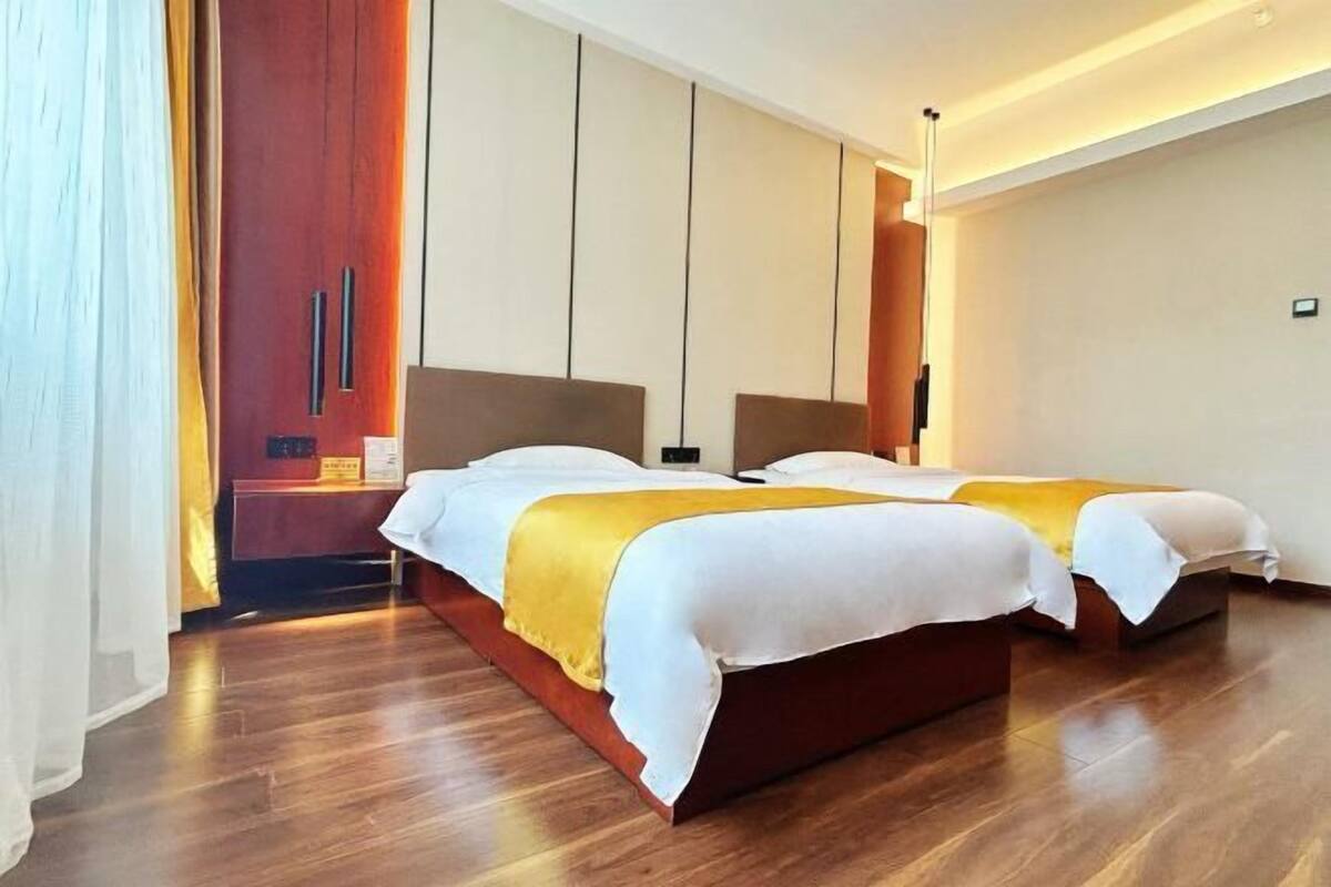 A hotel room with two beds, wooden flooring, a wardrobe, and a bedside table.