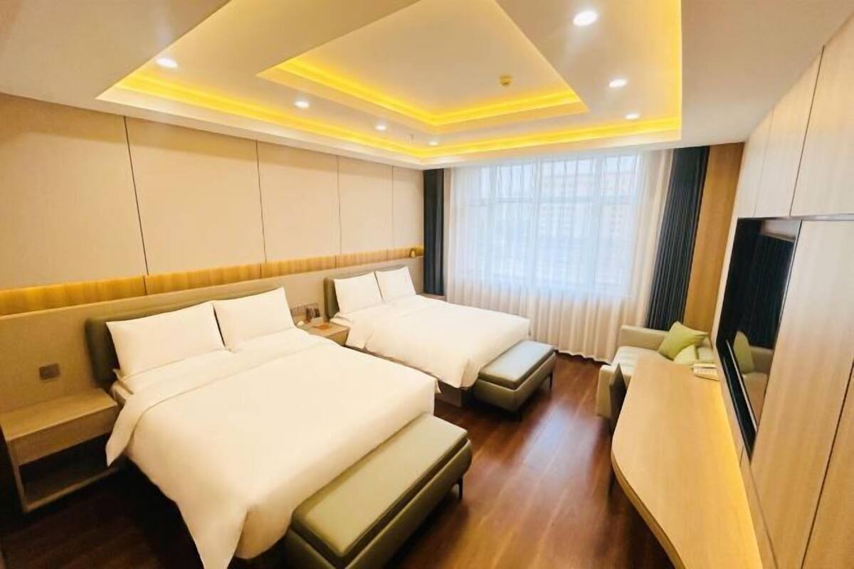 A hotel room with two beds, a bench, a TV, and a large window.
