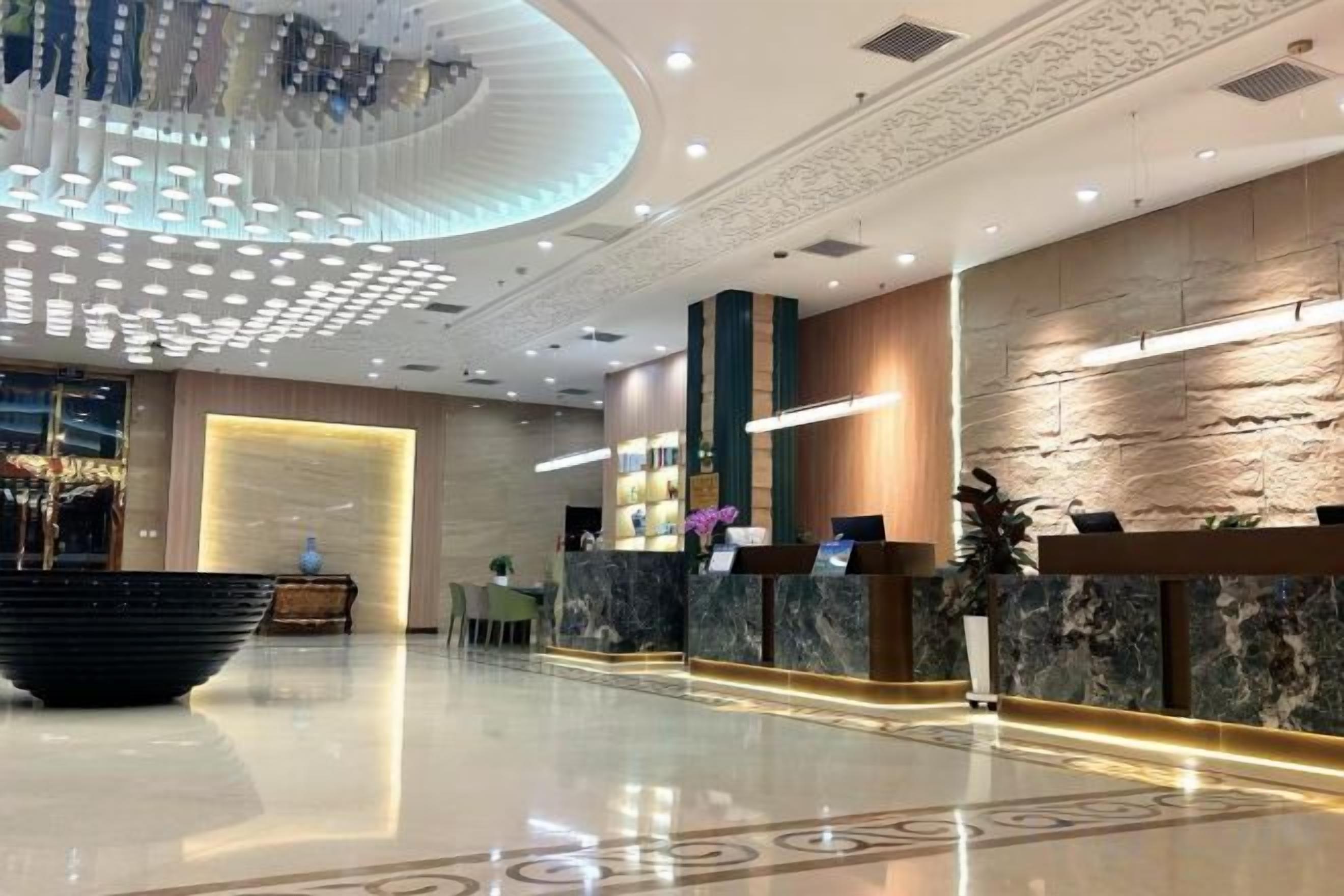 A modern hotel lobby with a reception desk, a large black bowl centerpiece, and a chandelier.