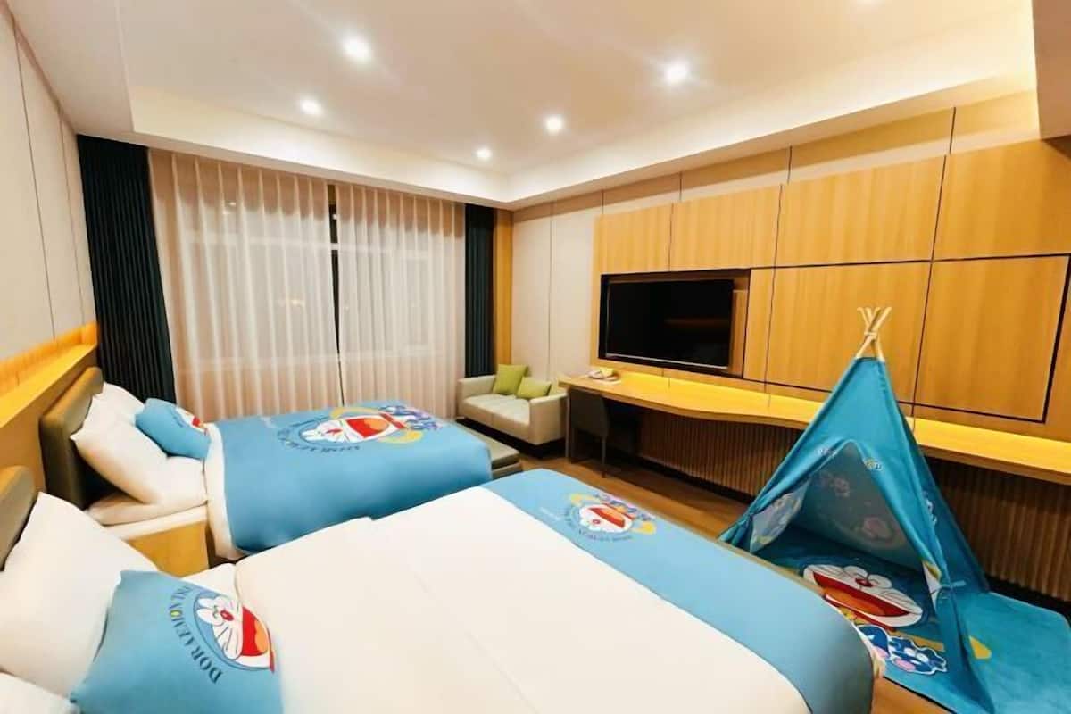 A hotel room with two beds, a TV, a desk, and a window with curtains.