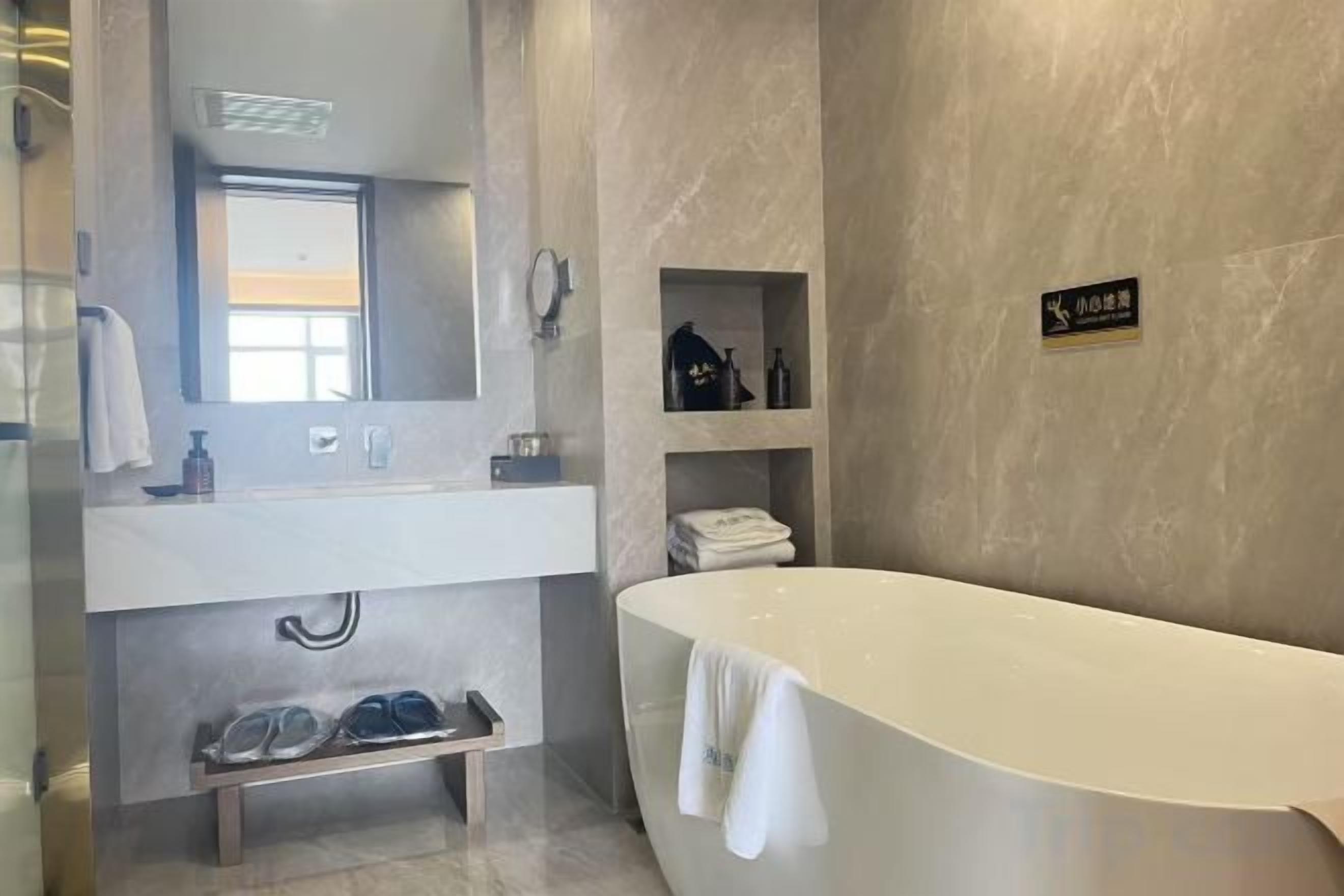Un baño moderno con una bañera grande, un lavamanos y un espejo. Hay estantes con artículos de aseo personal y un perchero para toallas.