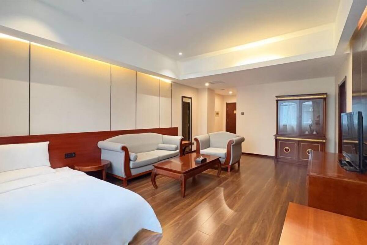 A hotel room with a bed, two sofas, a coffee table, a TV, and a wooden cabinet.