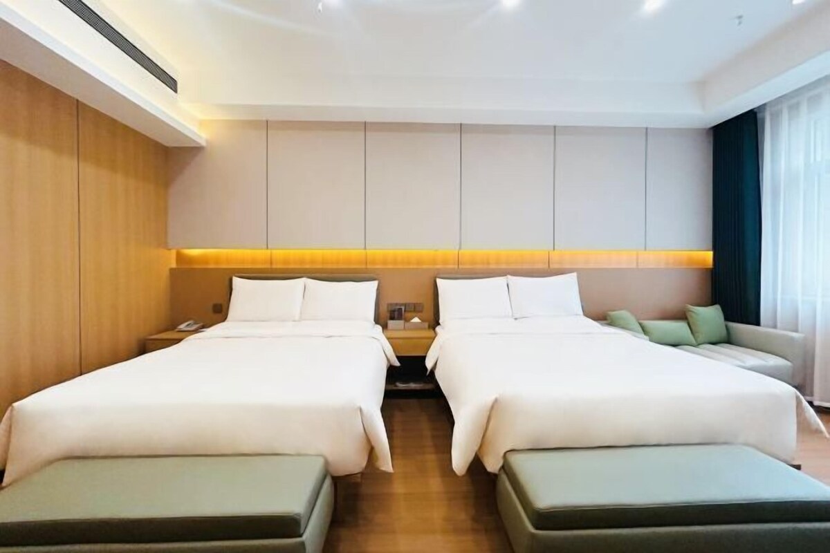 Une chambre d’hôtel avec deux lits, un canapé, une table de chevet et une grande fenêtre.