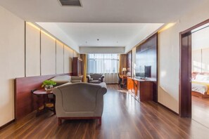 Une chambre d’hôtel comprenant un canapé, un fauteuil, une petite table avec une plante, un bureau avec une lampe et un lit.